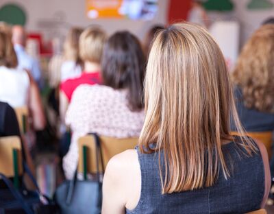 Klassenraum mit mehreren sitzenden, meist weiblichen Personen